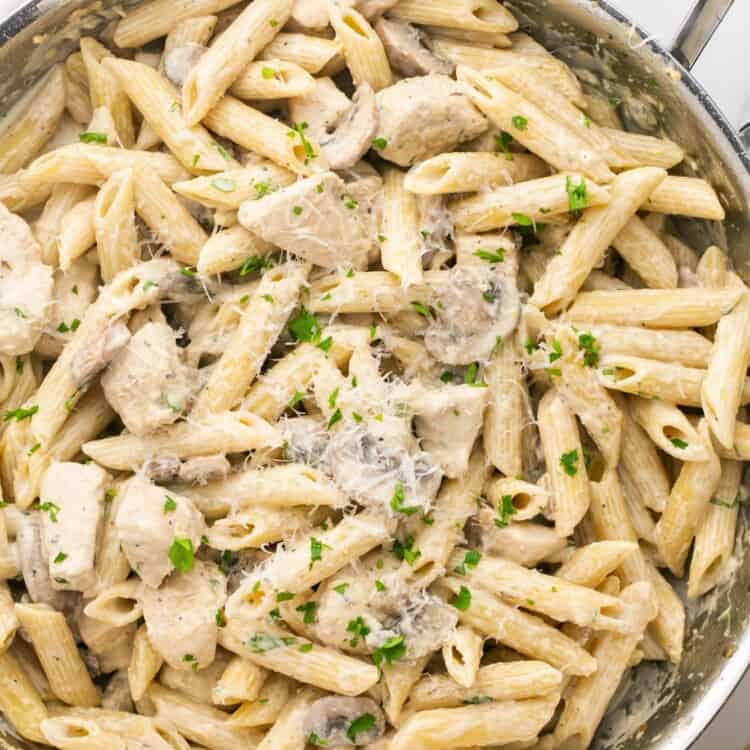 a stainless steel skillet with two handles, filled with penne with chicken and mushrooms in a creamy sauce.