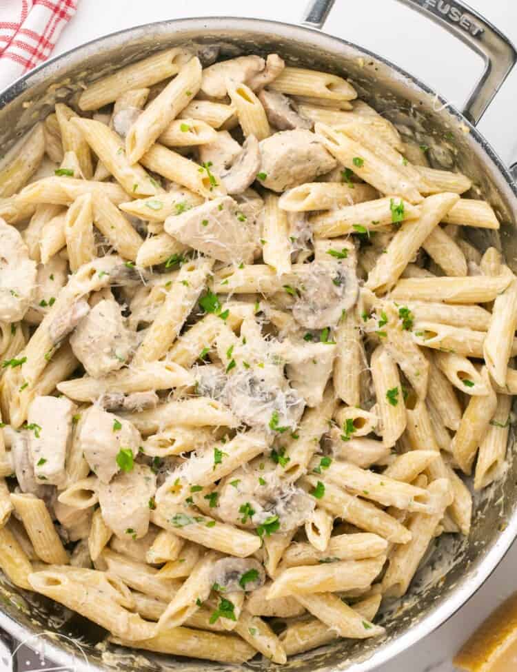 a stainless steel skillet with two handles, filled with penne with chicken and mushrooms in a creamy sauce.