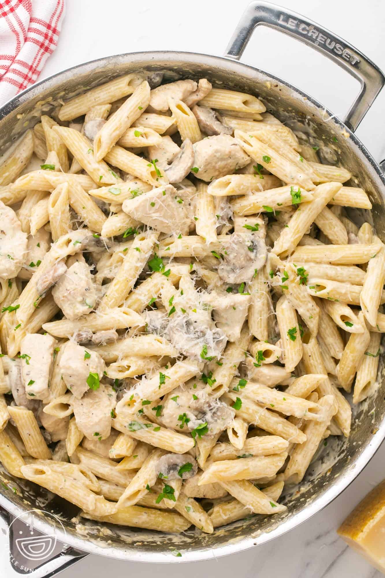 a stainless steel skillet with two handles, filled with penne with chicken and mushrooms in a creamy sauce. 