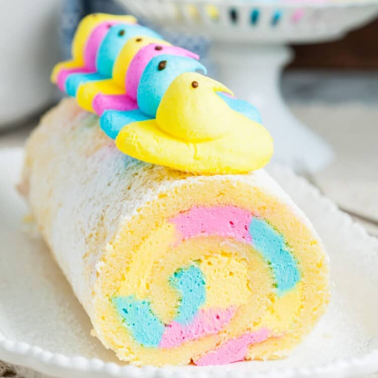 a vanilla cake roll with pink, blue, and yellow icing inside, topped with chicks peeps.
