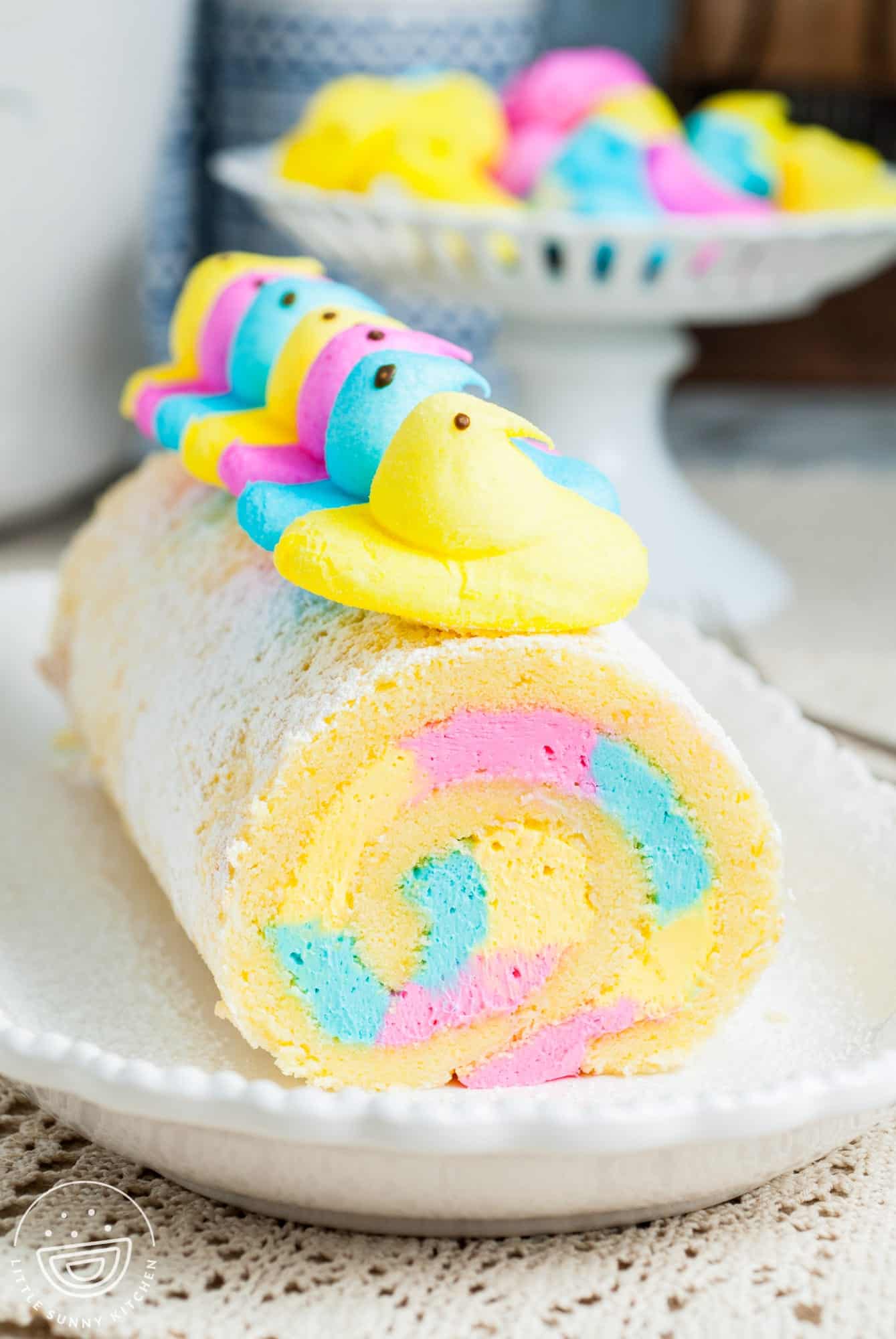 a vanilla cake roll with pink, blue, and yellow icing inside, topped with chicks peeps.