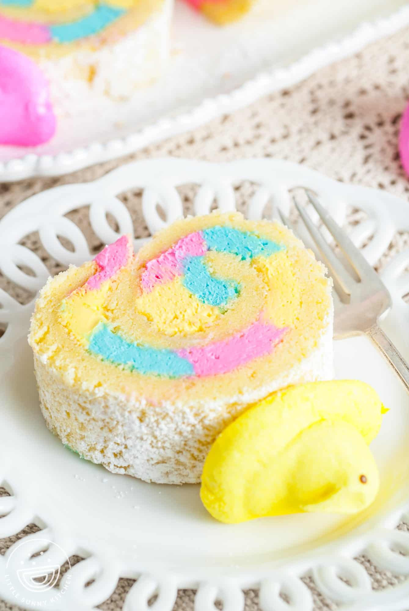 a slice of a cake roll with pink, blue, and yellow frosting and a yellow peep on top.
