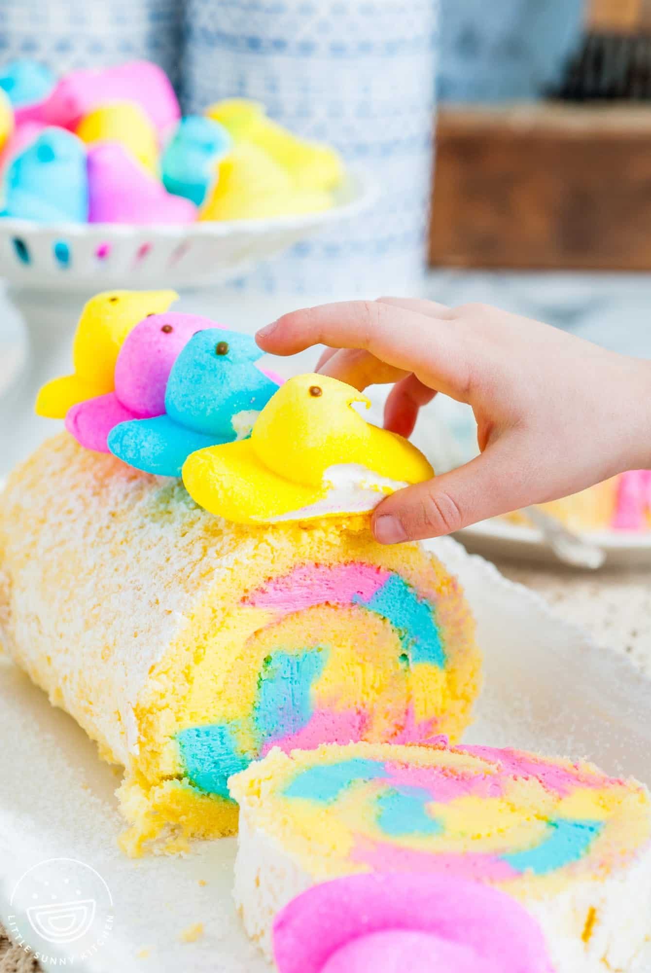 a hand arranging peeps on top of an easter colored cake roll.