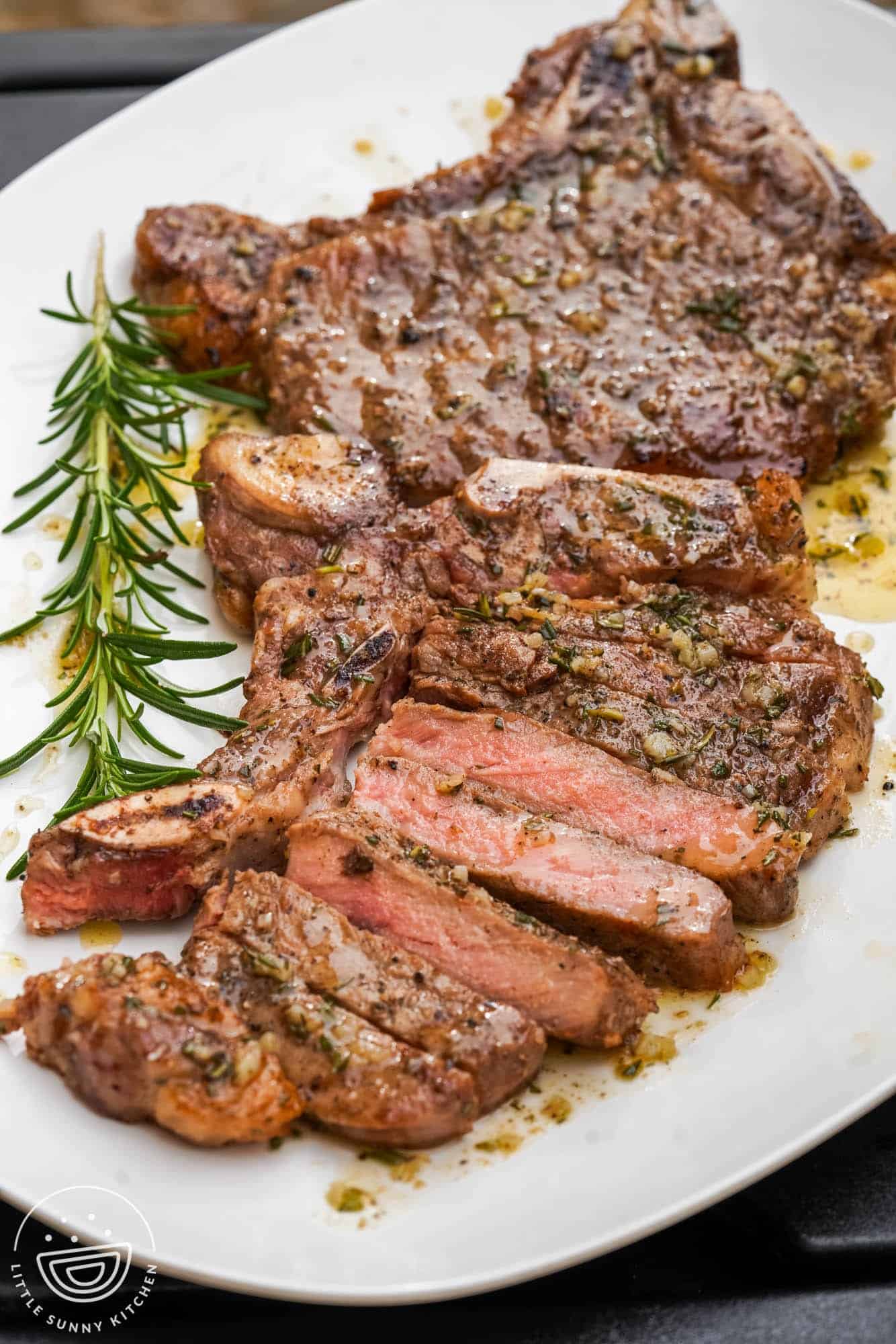 a platter holding grilled steaks, garnished with a sprig of rosemary.