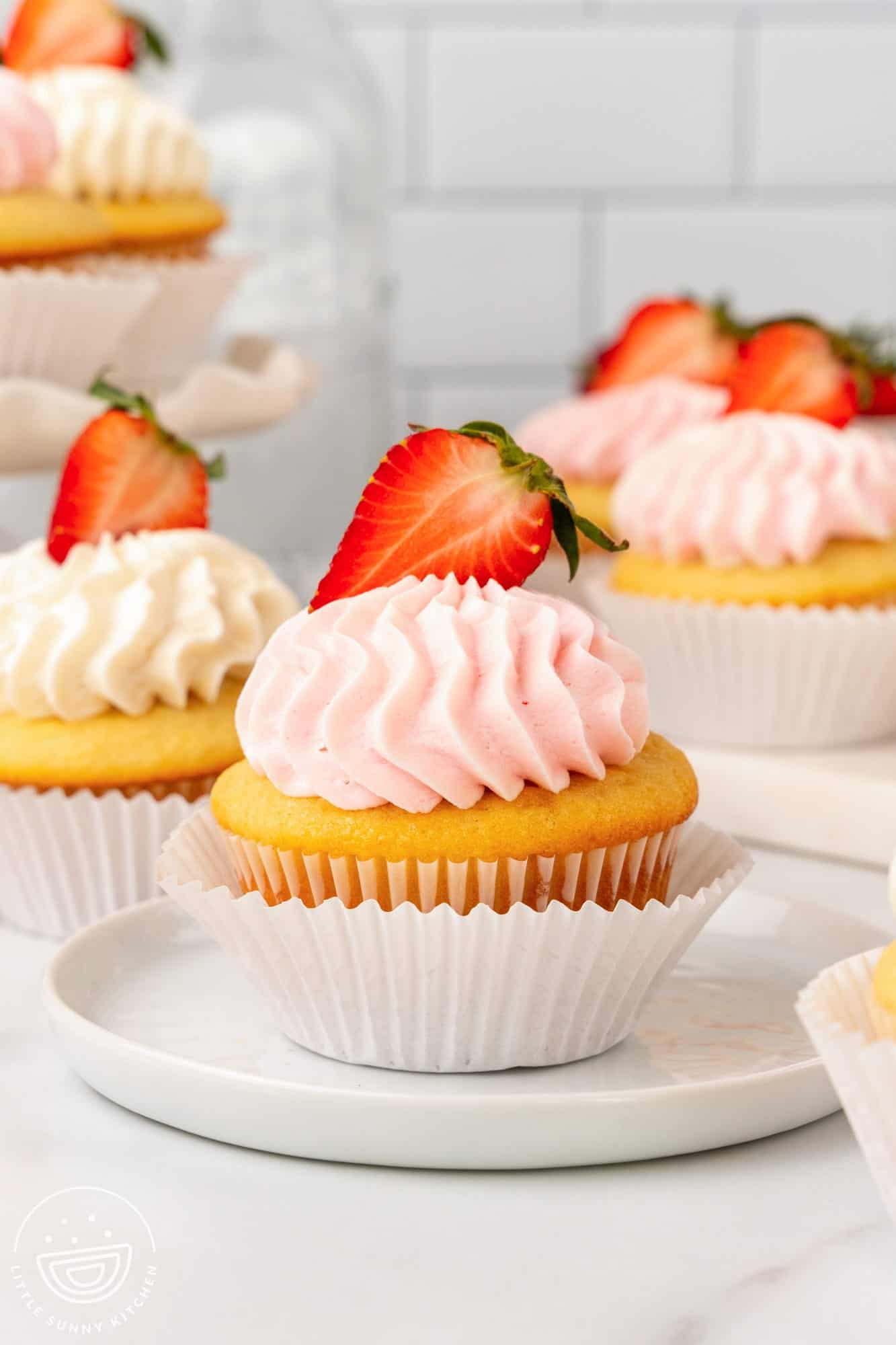 Jam filled cupcake with strawberry and frosting in a double liner on a small plate.