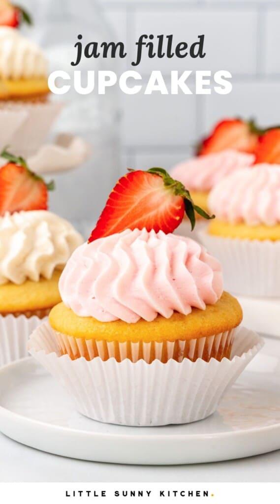 Jam filled cupcake with strawberry and frosting in a double liner on a small plate. text overlay says "jam filled cupcakes"
