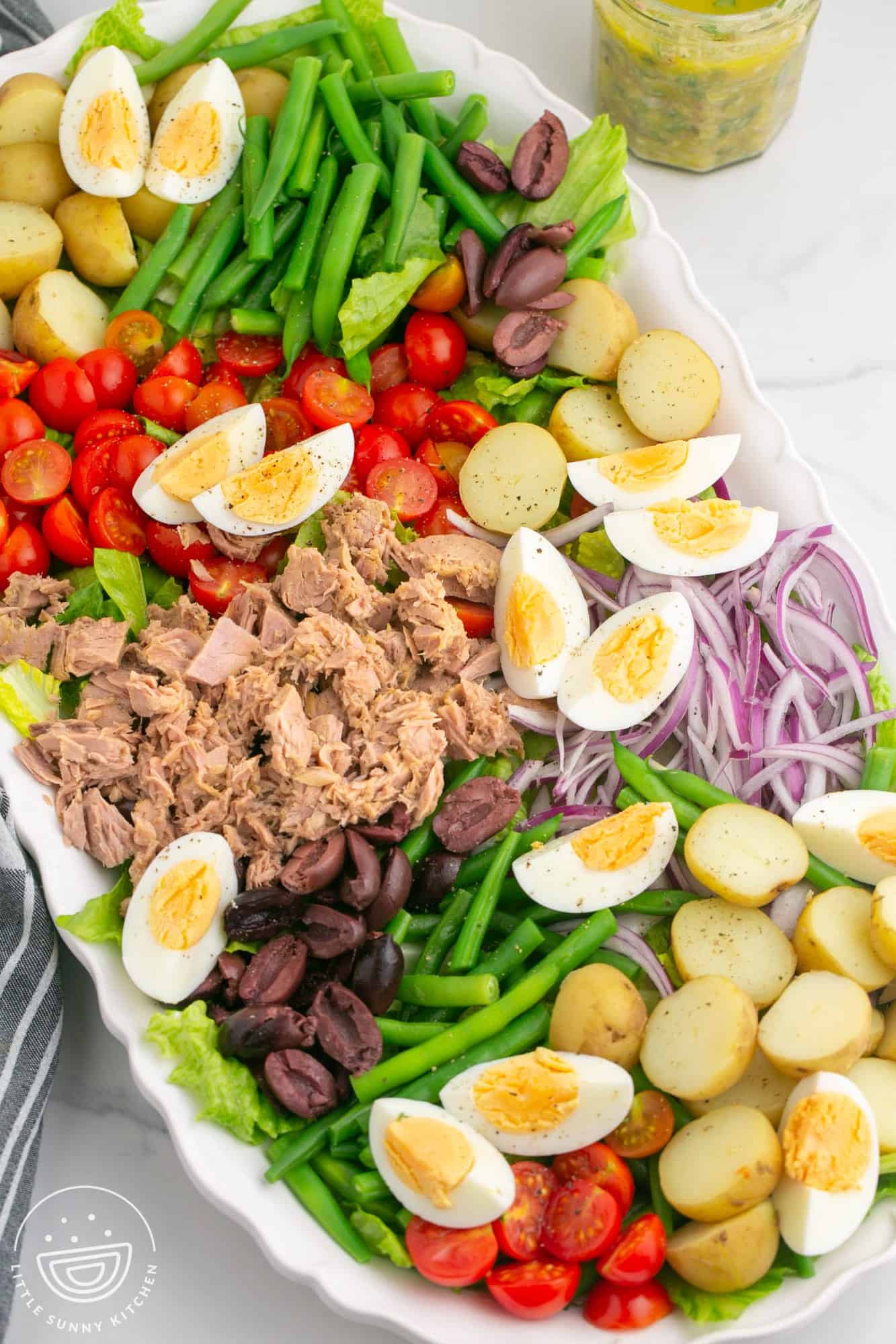 a large nicoise salad with eggs, potatoes, tuna, and green beans on an oval platter. 