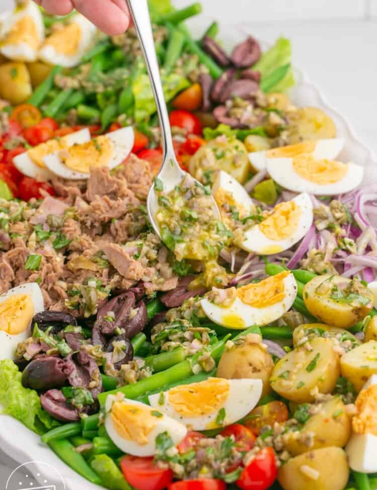 dressing being spooned over a plated nicoise salad