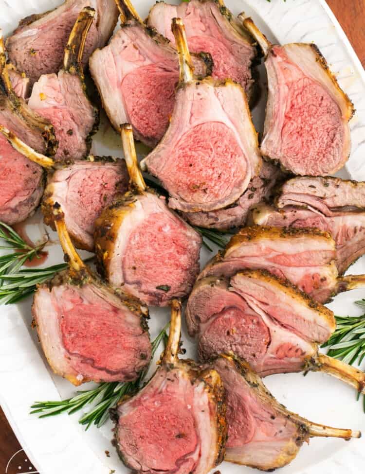 Sliced rack of lamb served on a platter, with fresh rosemary leaves.