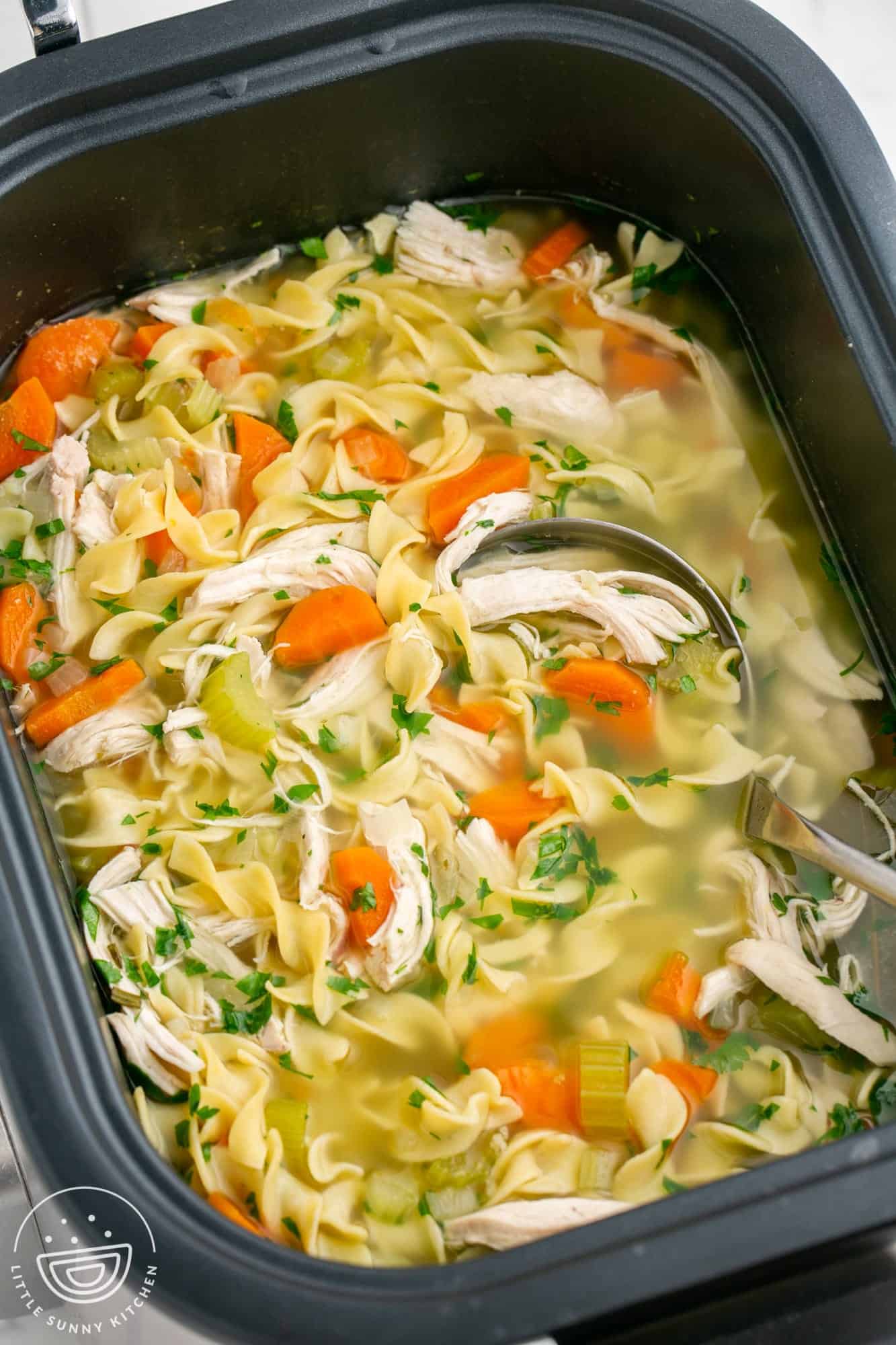 Chicken noodle soup in a large rectangular slow cooker.