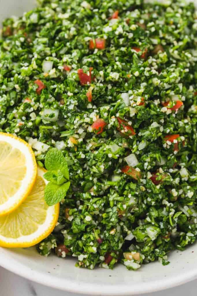 a large bowl of traditionally made tabbouleh salad with lemon slices on the side.