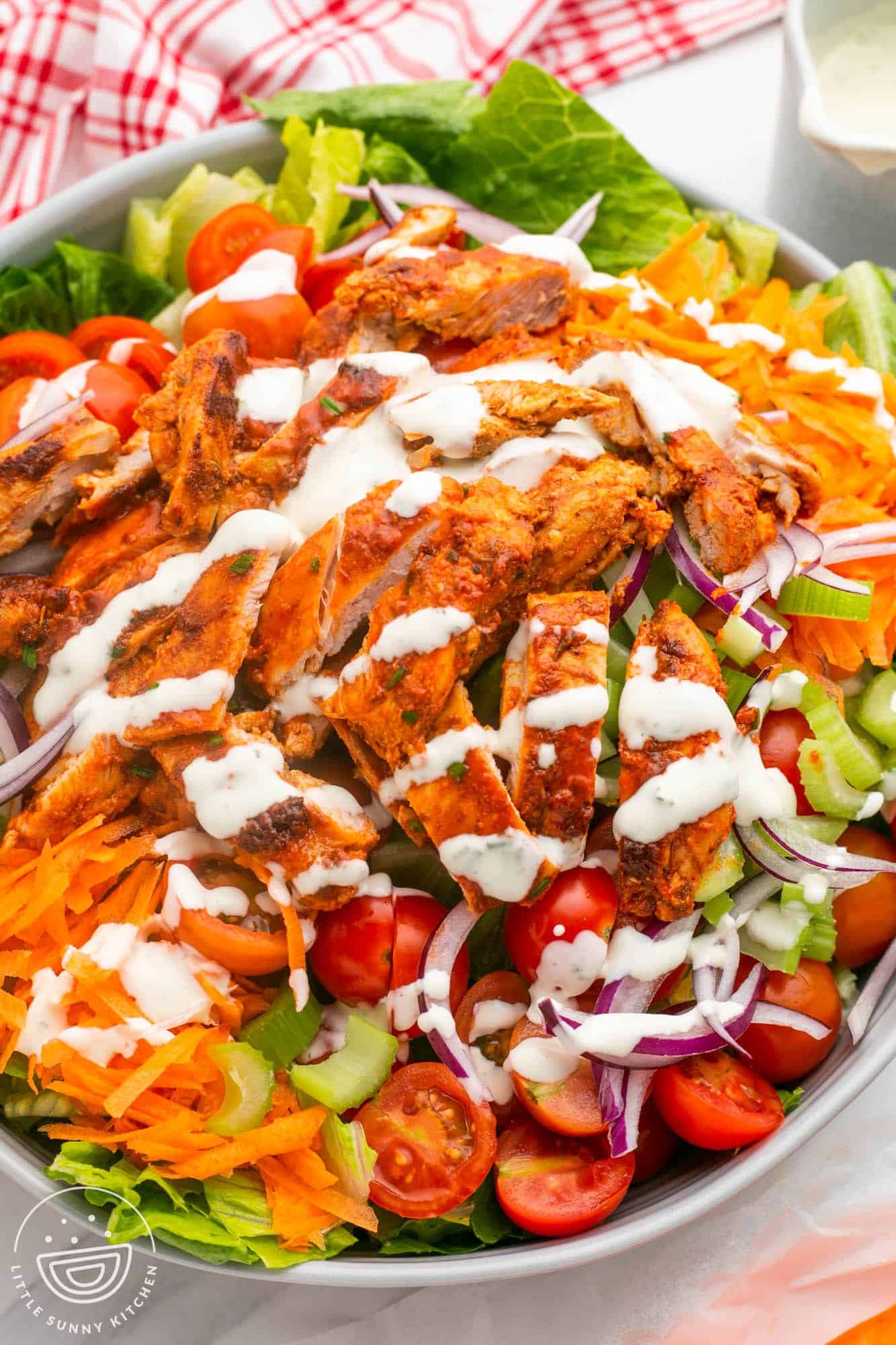A large white bowl of salad with buffalo chicken cut into strips, and ranch dressing.