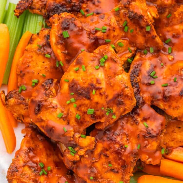 a pile of buffalo chicken thighs on a platter with celery sticks.