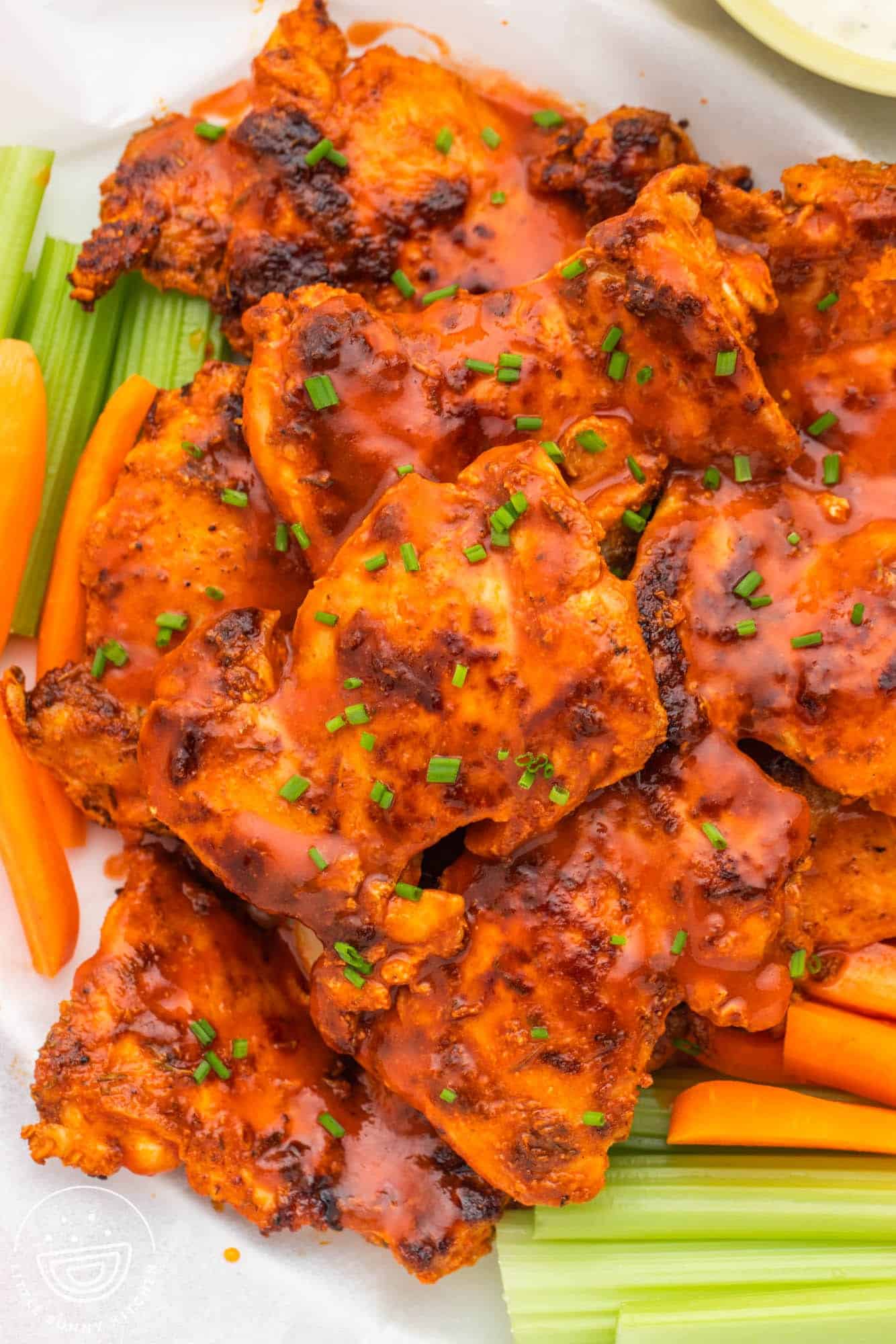 a pile of buffalo chicken thighs on a platter with celery sticks.