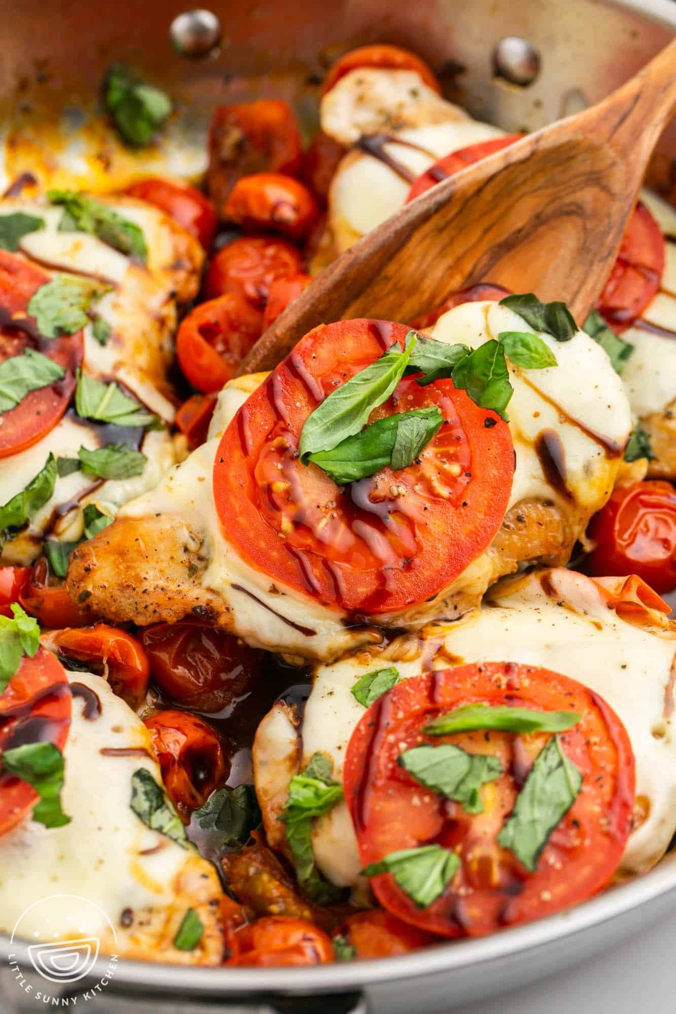 closeup of chicken cutlets with caprese toppings including mozzarella, tomato slices, basil and a drizzle of balsamic. 