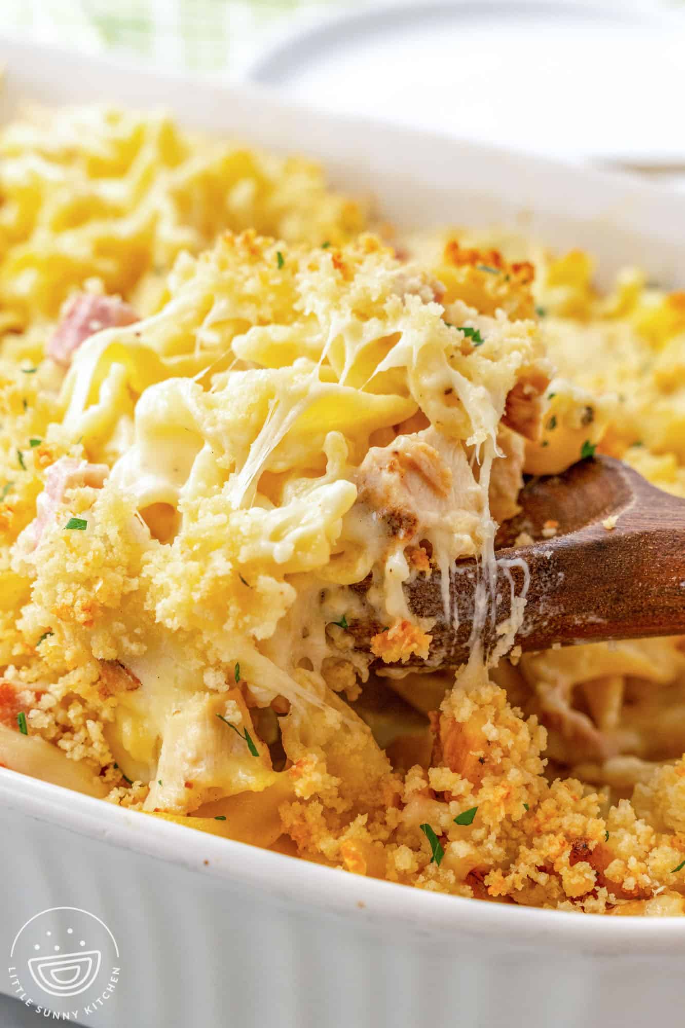 Serving Chicken Cordon Bleu Casserole from the dish with a wooden serving spoon, showing the cheesy creamy textures