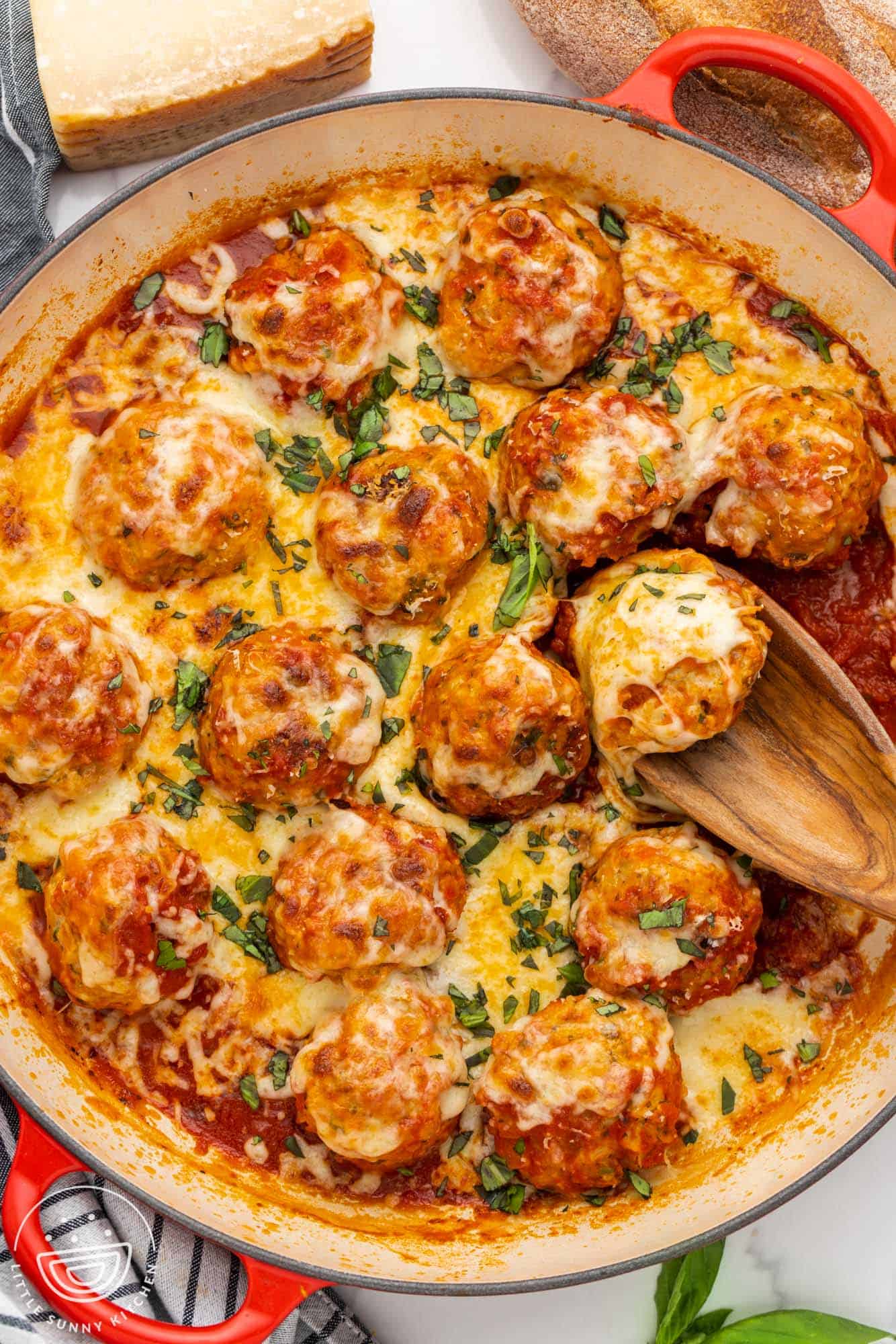 A round skillet of chicken parmesan meatballs in sauce, topped with cheese.