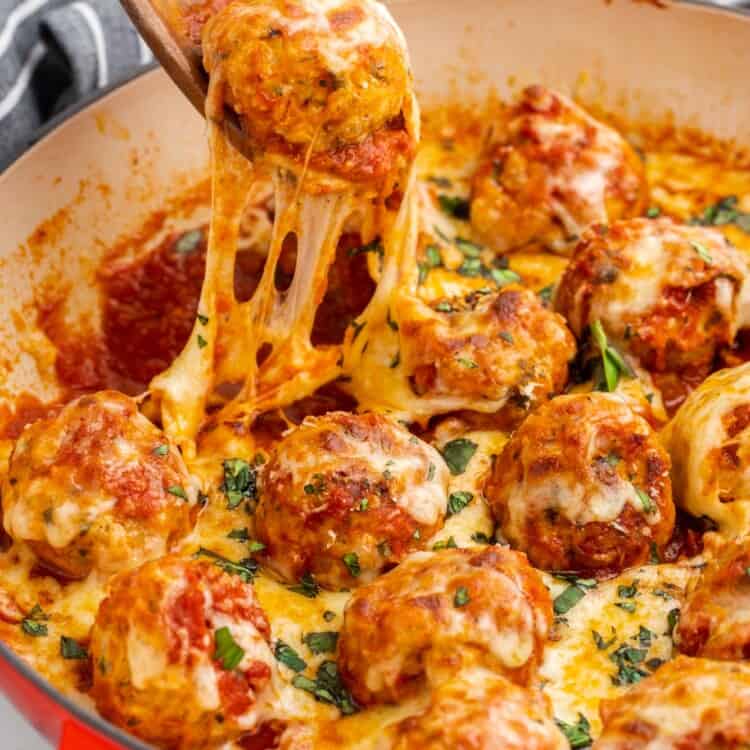 a spoon lifting a chicken parm meatball out of a skillet, with stringy mozzarella cheese melt.