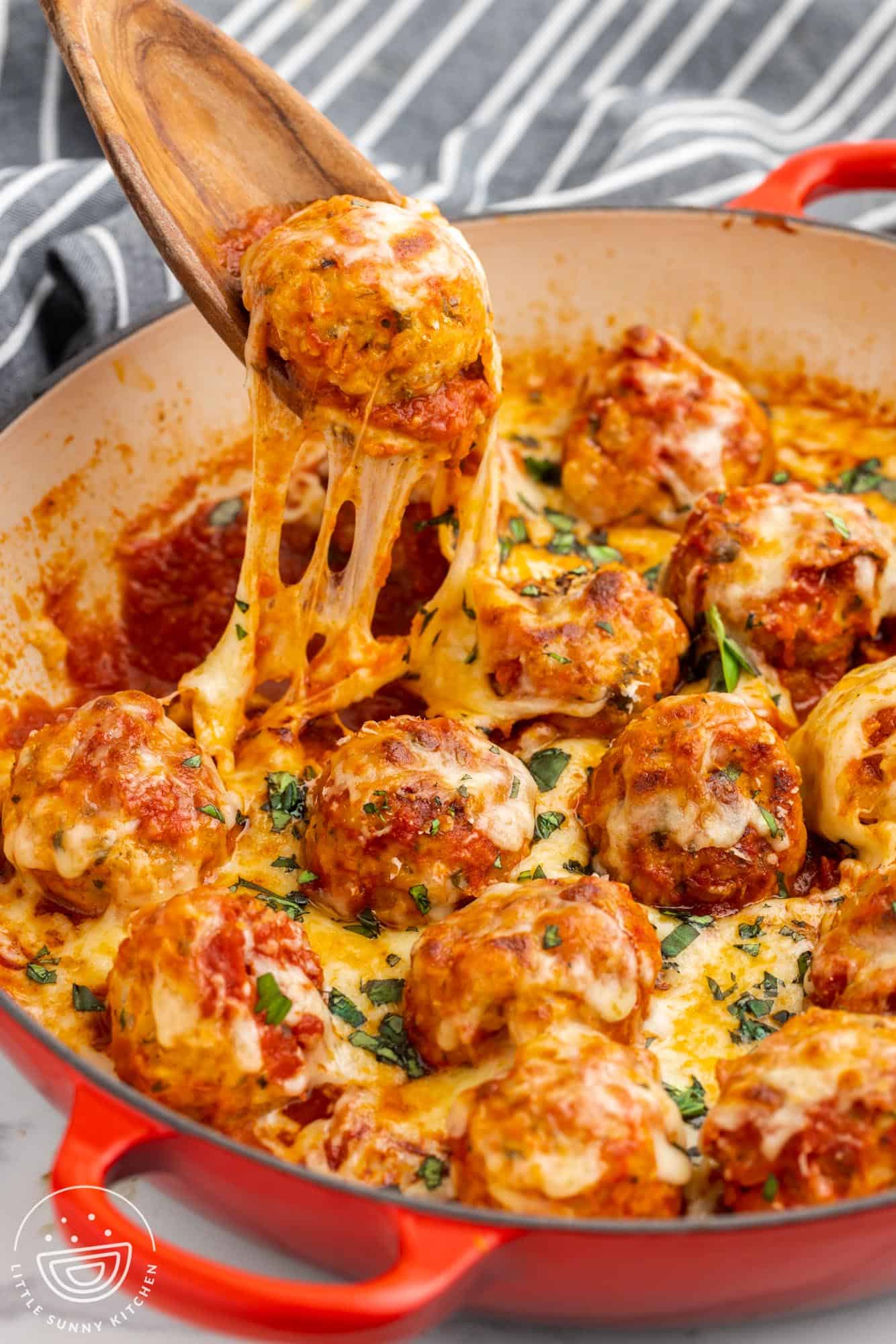 a spoon lifting a chicken parm meatball out of a skillet, with stringy mozzarella cheese melt.