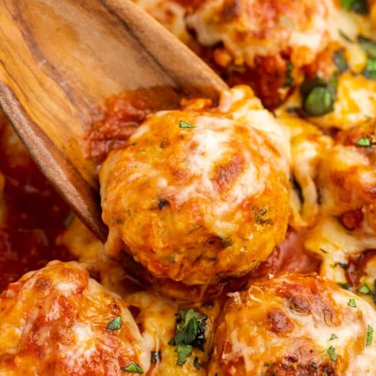 closeup of cheesy chicken parmesan meatballs, served with a wooden spoon.