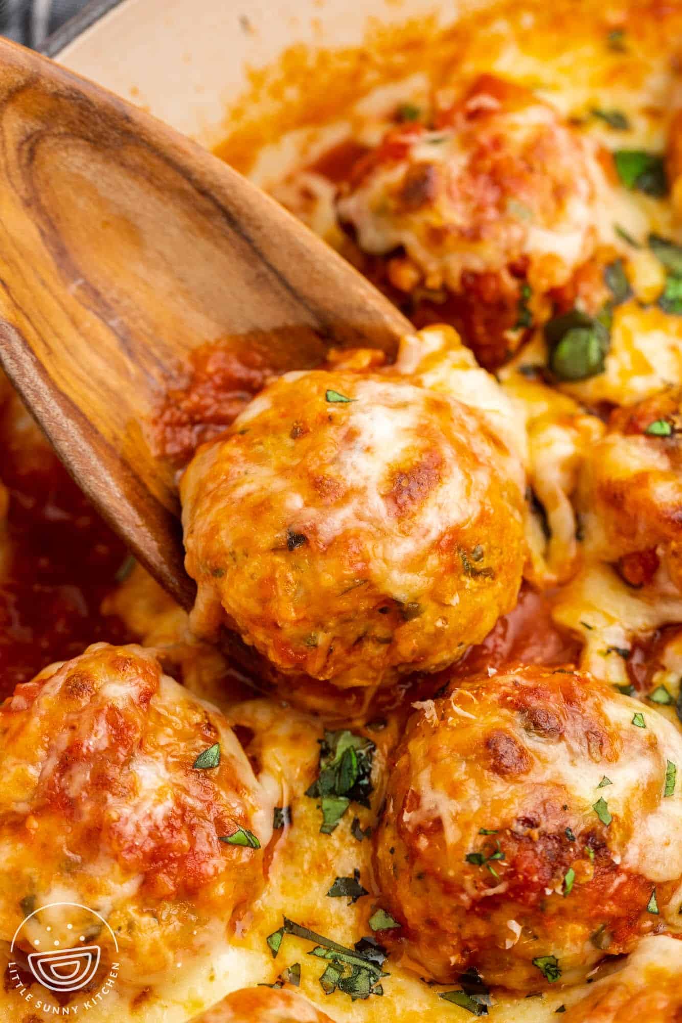 closeup of cheesy chicken parmesan meatballs, served with a wooden spoon. 