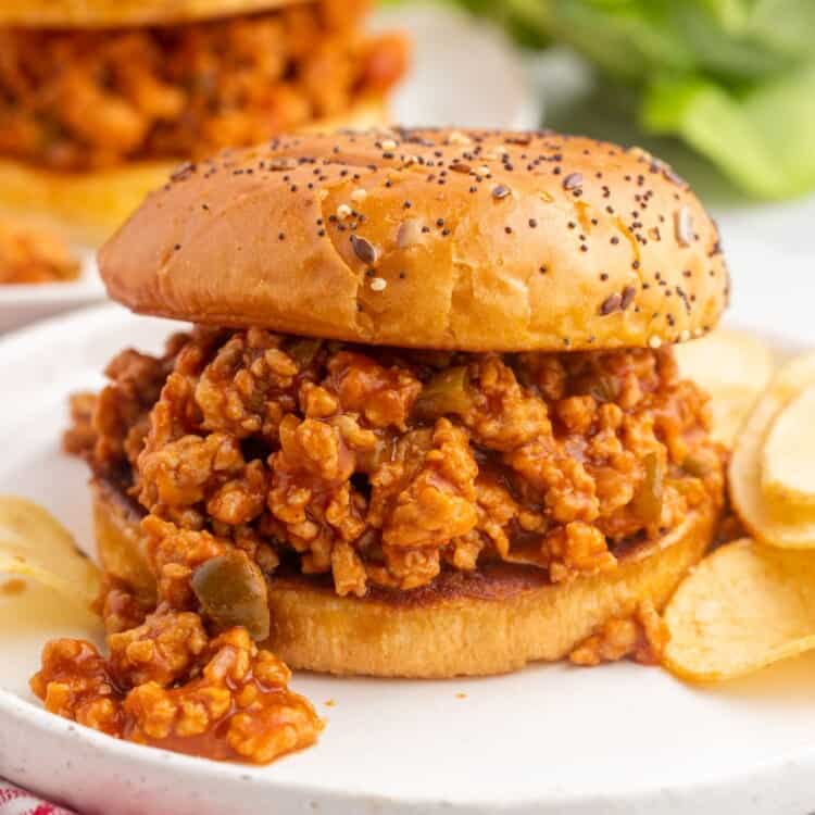 a sloppy joe sandwich made with ground chicken on a seeded bun. The sandwich is on a plate with chips on the side.