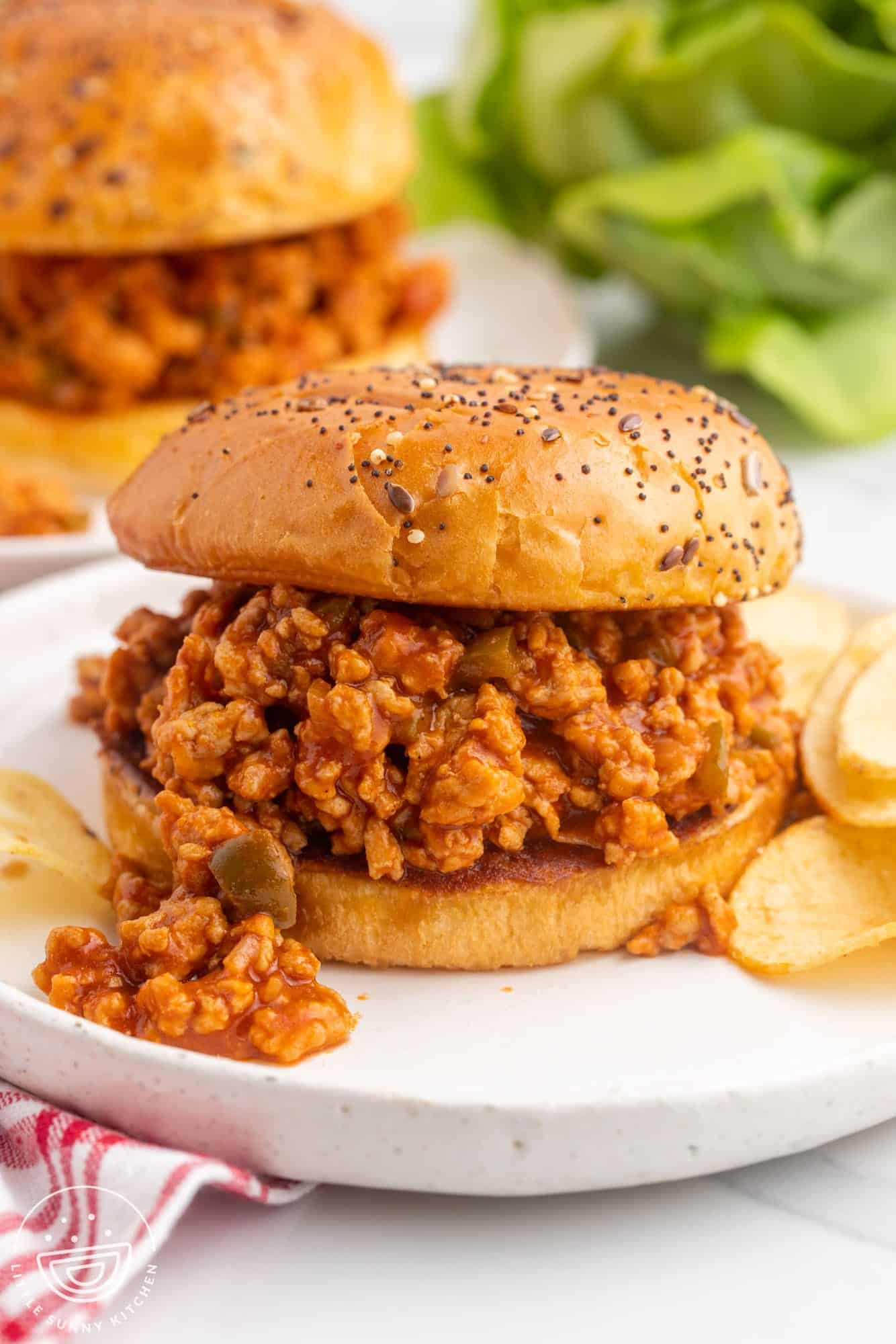 a sloppy joe sandwich made with ground chicken on a seeded bun. The sandwich is on a plate with chips on the side. 