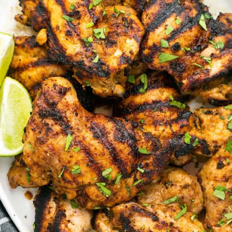 A platter of grilled cilantro lime chicken thighs with lime wedges.