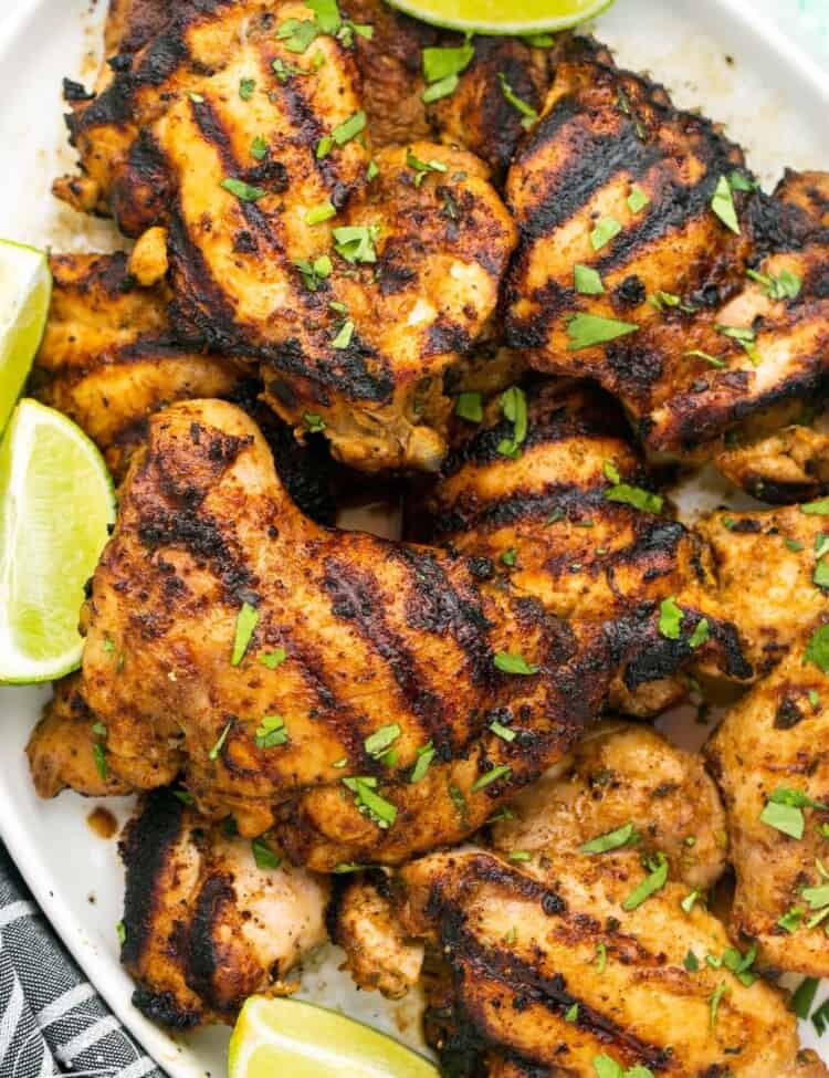 A platter of grilled cilantro lime chicken thighs with lime wedges.