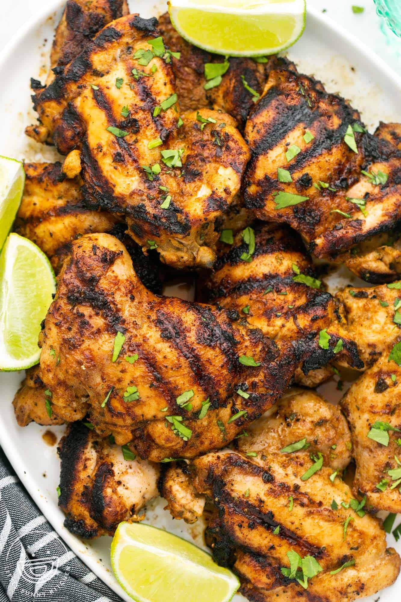 A platter of grilled cilantro lime chicken thighs with lime wedges. 