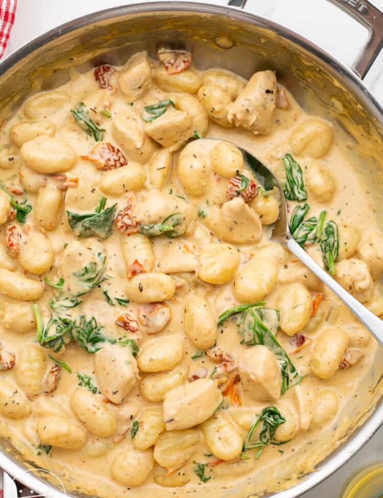 a large skillet of creamy gnocchi with chicken and spinach.