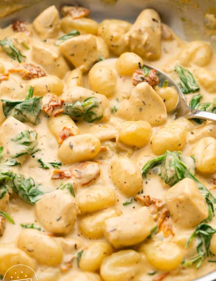 Gnocchi in a skillet in a creamy spinach sauce with pieces of chicken.