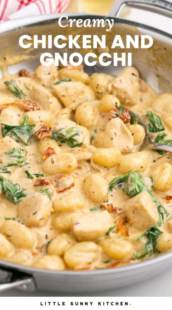 a stainless steel skillet of gnocchi with chicken and spinach in a creamy sauce. Text overlay says "creamy chicken and gnocchi"