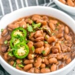 Pinto beans in a medium sized white bowl, topped with sliced jalapeno and cilantro