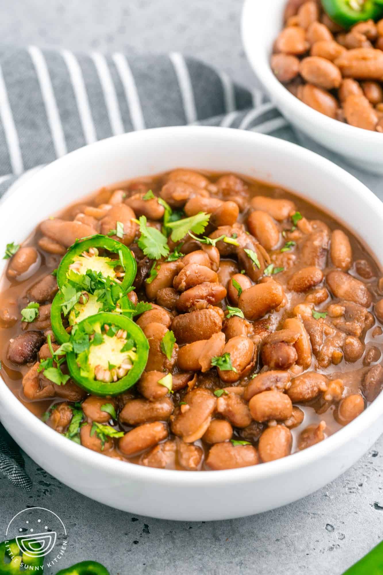 Pinto beans in a medium sized white bowl, topped with sliced jalapeno and cilantro