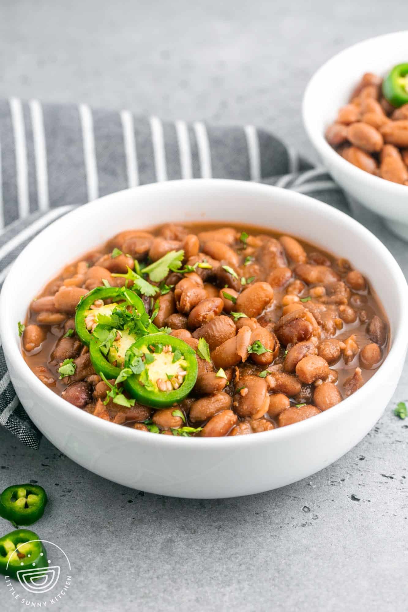 Pinto beans in a medium sized white bowl, topped with sliced jalapeno and cilantro