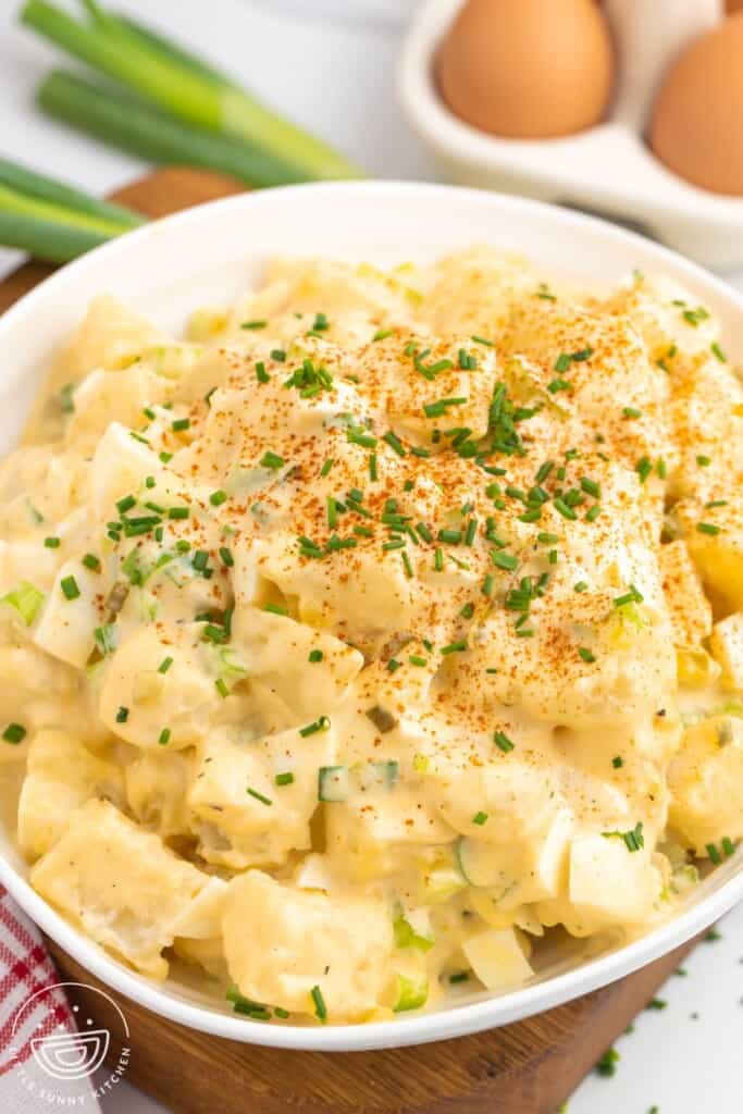 a large bowl of potato salad. In the background are brown eggs and green onions.