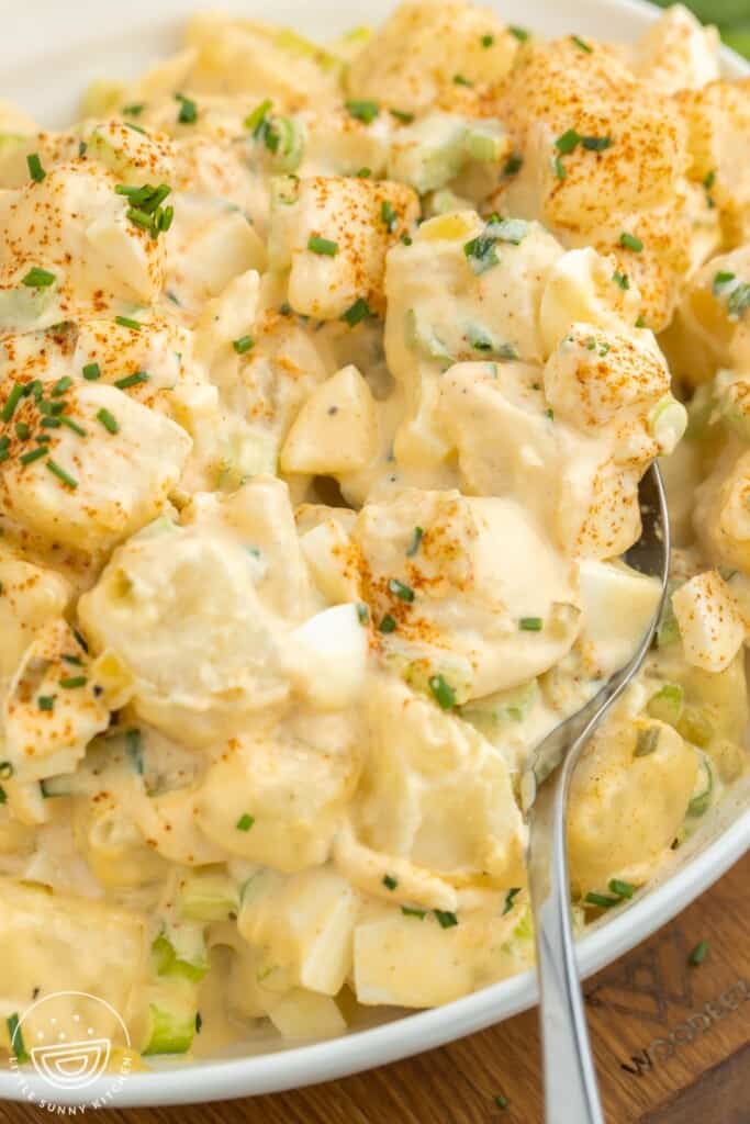 closeup view of a bowl of deviled egg potato salad with a serving spoon.