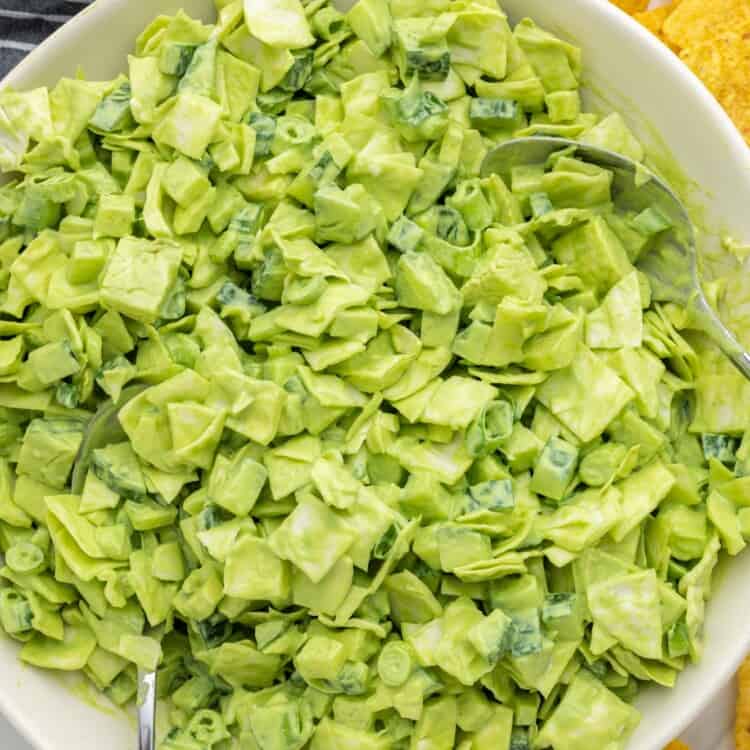 Overhead shot of a large white bowl with green chopped salad, and tortilla chips on the sides.