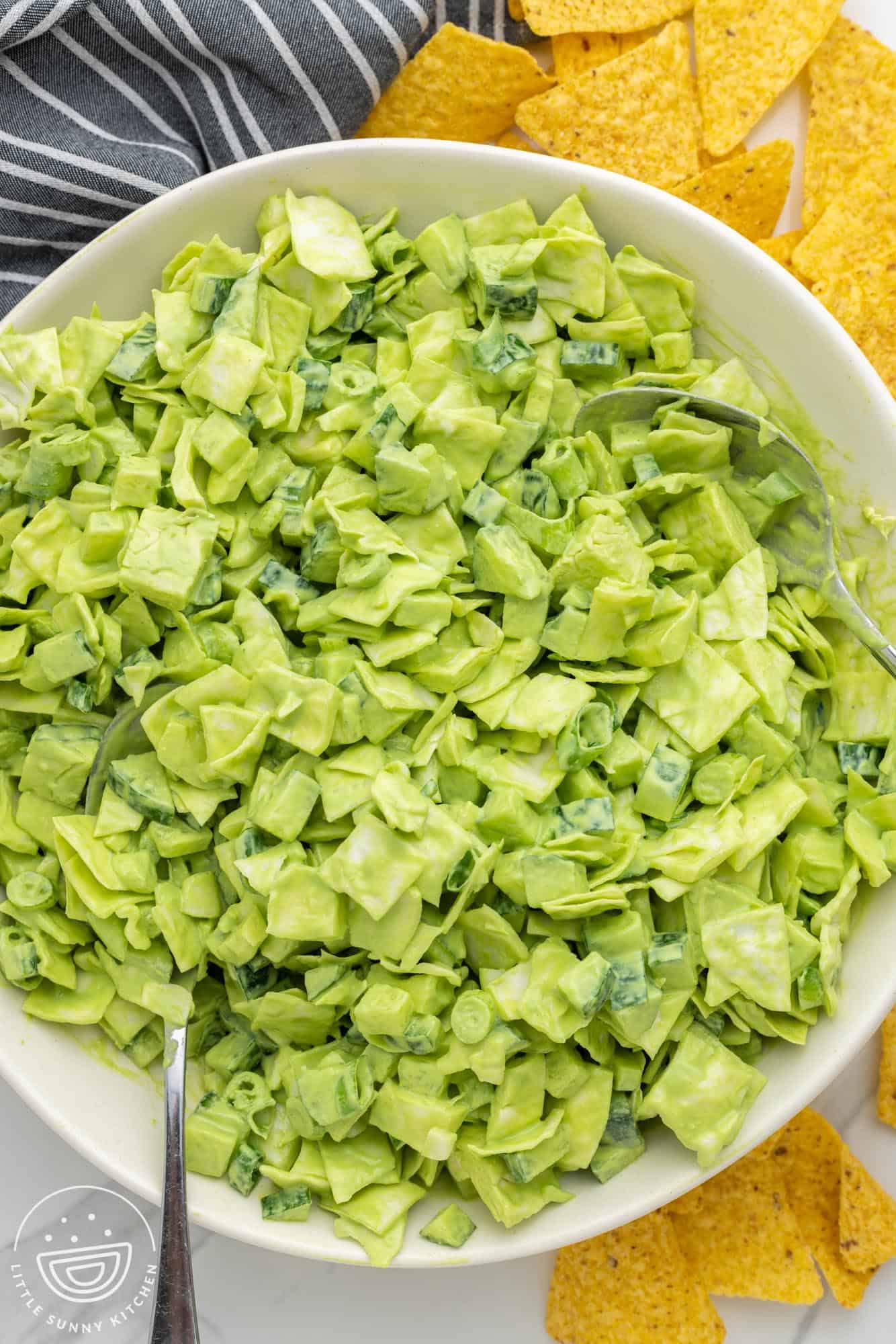 Overhead shot of a large white bowl with green chopped salad, and tortilla chips on the sides.