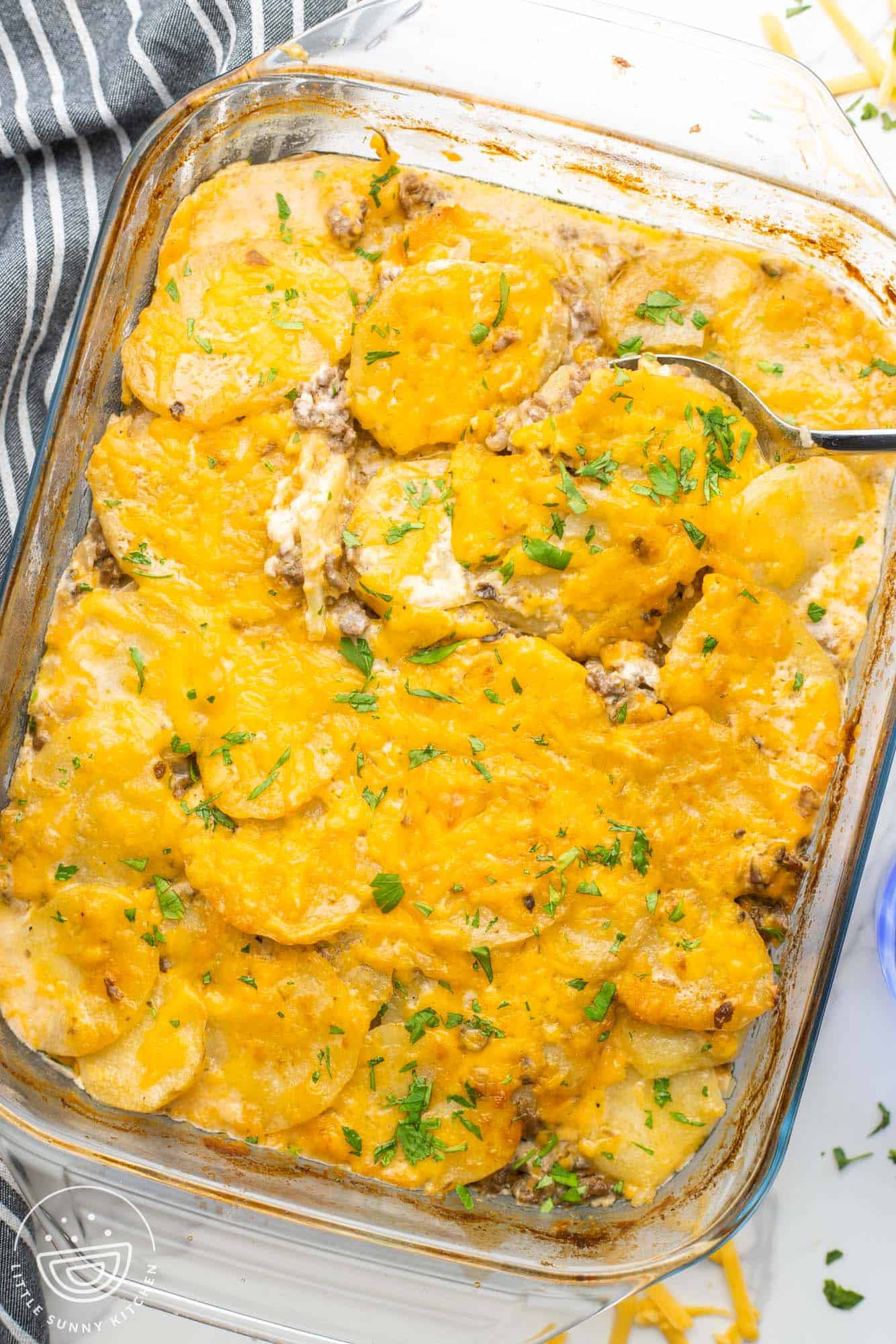 a glass 9x13 inch baking dish filled with potato and hamburger casserole, topped with melted cheese and fresh parsley.