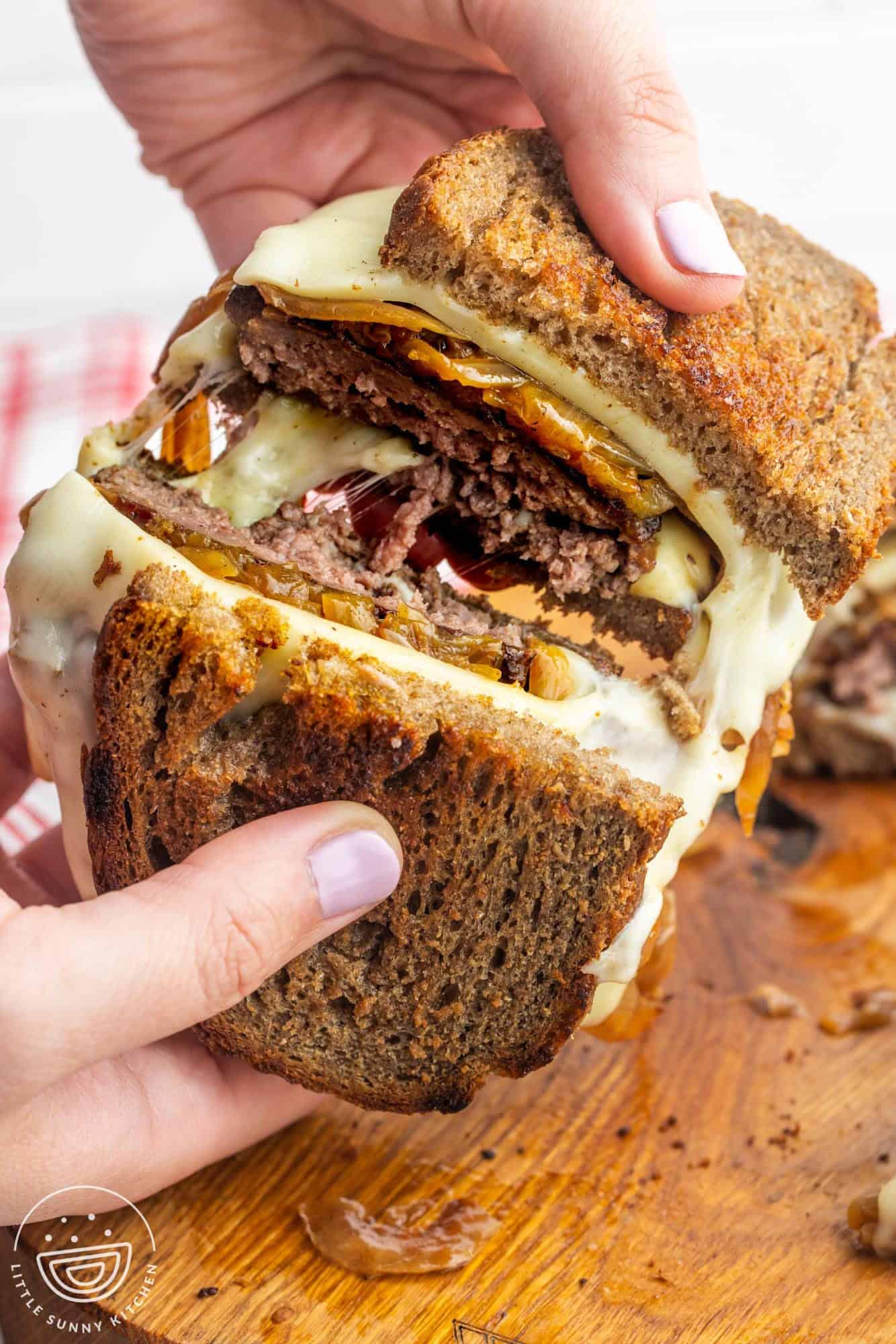 a patty melt cut in half and pulled apart by two hands to show melty cheese and caramelized onions inside.