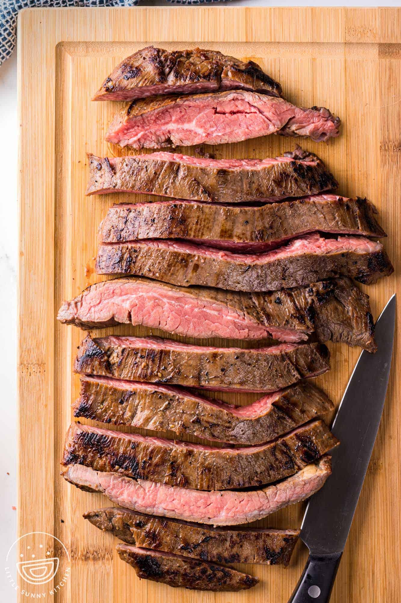 Sliced flank steak on a wooden cutting board and a knife