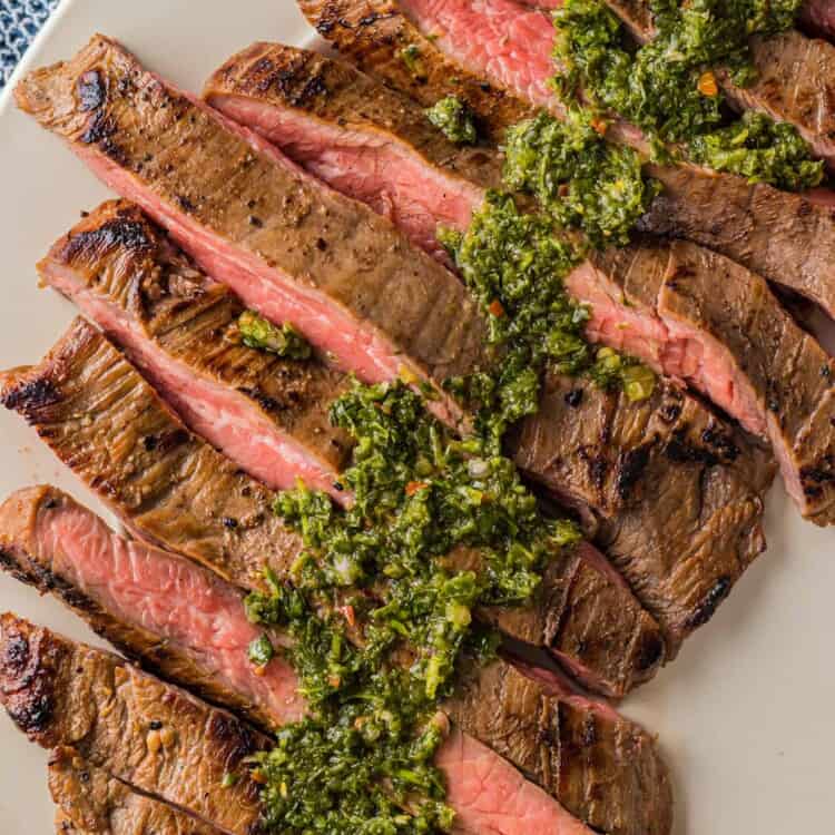 Overhead shot of sliced smoked flank steak, topped with fresh chimichurri sauce