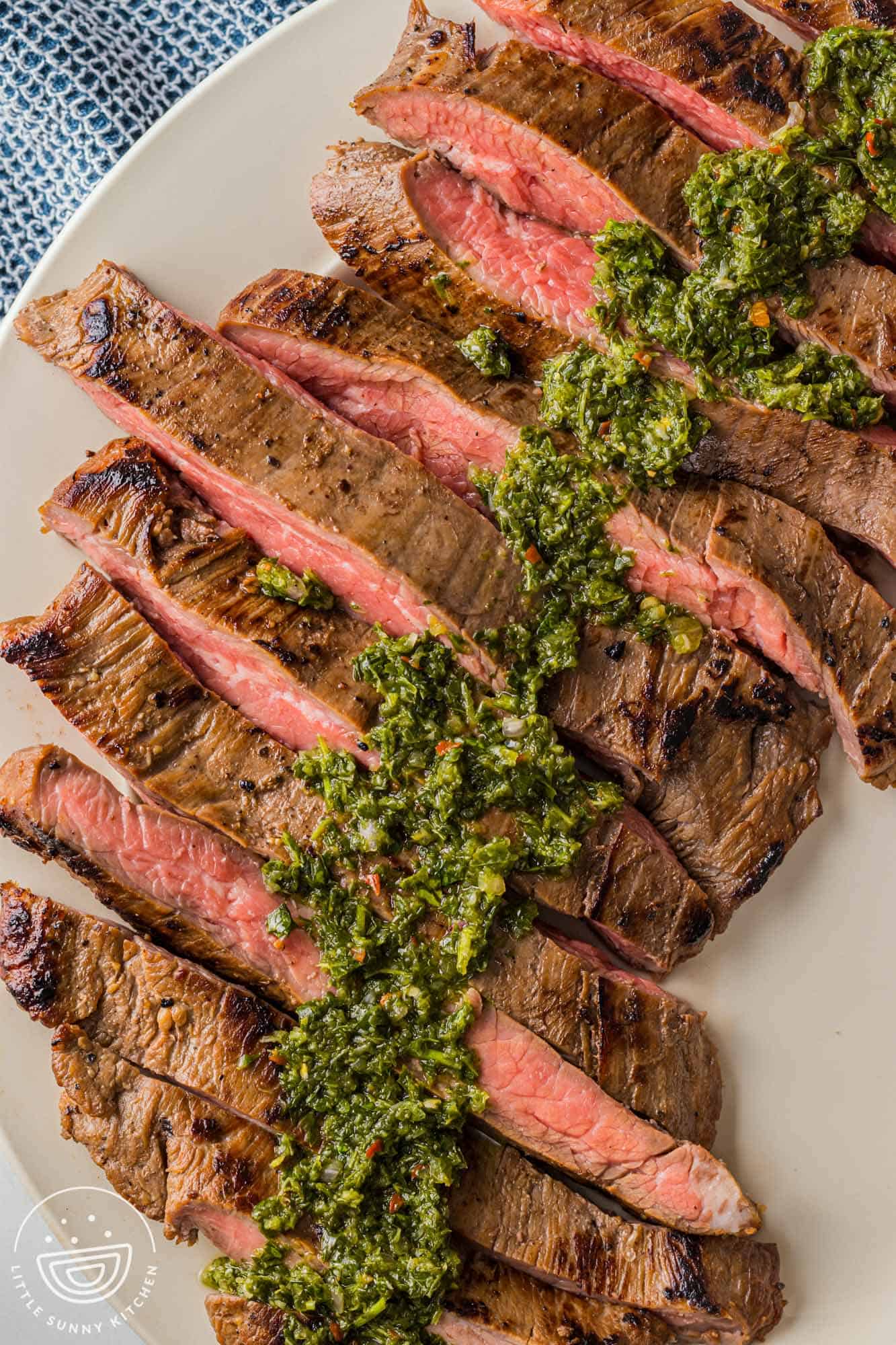 Overhead shot of sliced smoked flank steak, topped with fresh chimichurri sauce