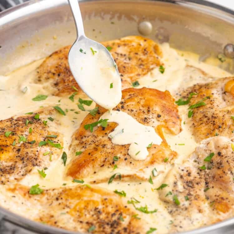 a stainless steel skillet with creamy tarragon chicken in it. A spoon is adding more sauce to one piece.