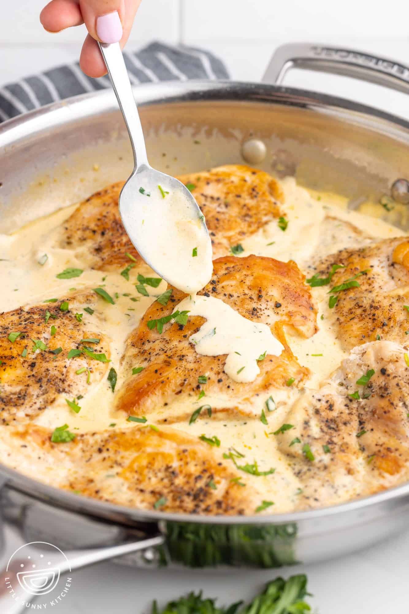 a stainless steel skillet with creamy tarragon chicken in it. A spoon is adding more sauce to one piece. 