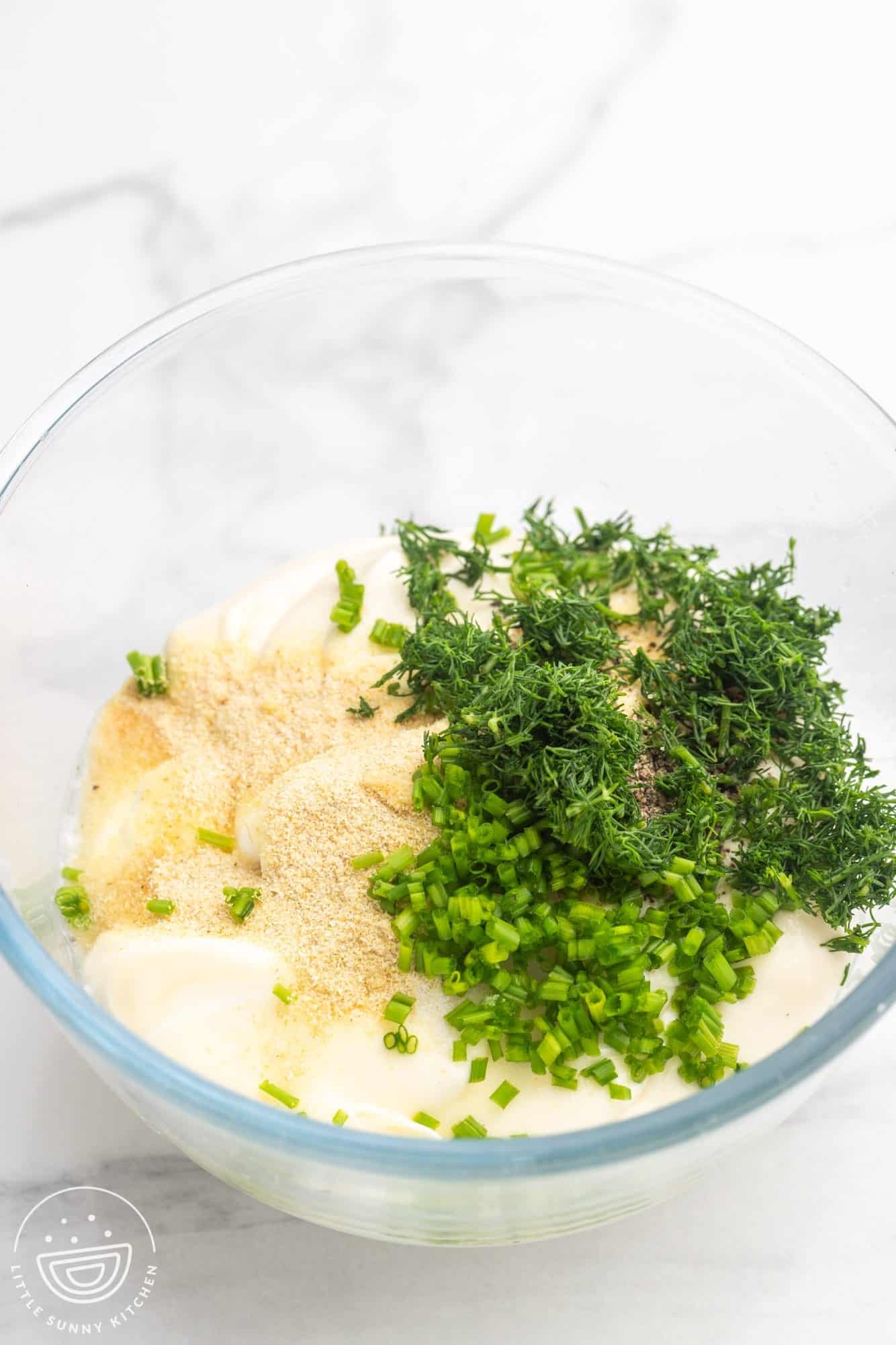 sour cream, mayo, herbs and seasonings in a glass mixing bowl.