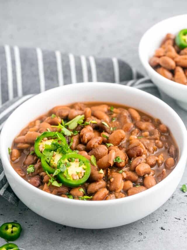 Pinto beans in a medium sized white bowl, topped with sliced jalapeno and cilantro