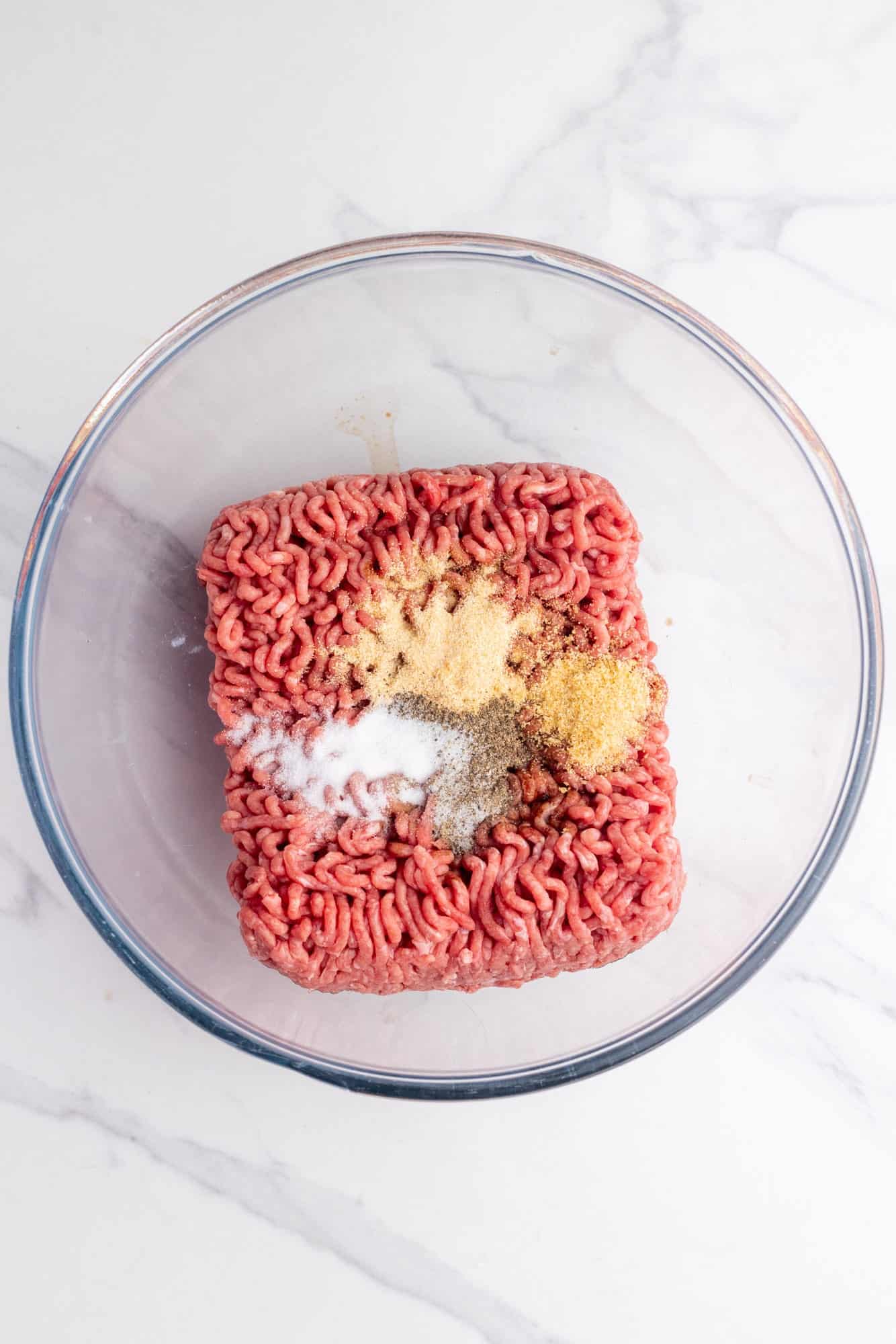Ground beef in a glass bowl topped with garlic powder, onion powder, salt and black pepper